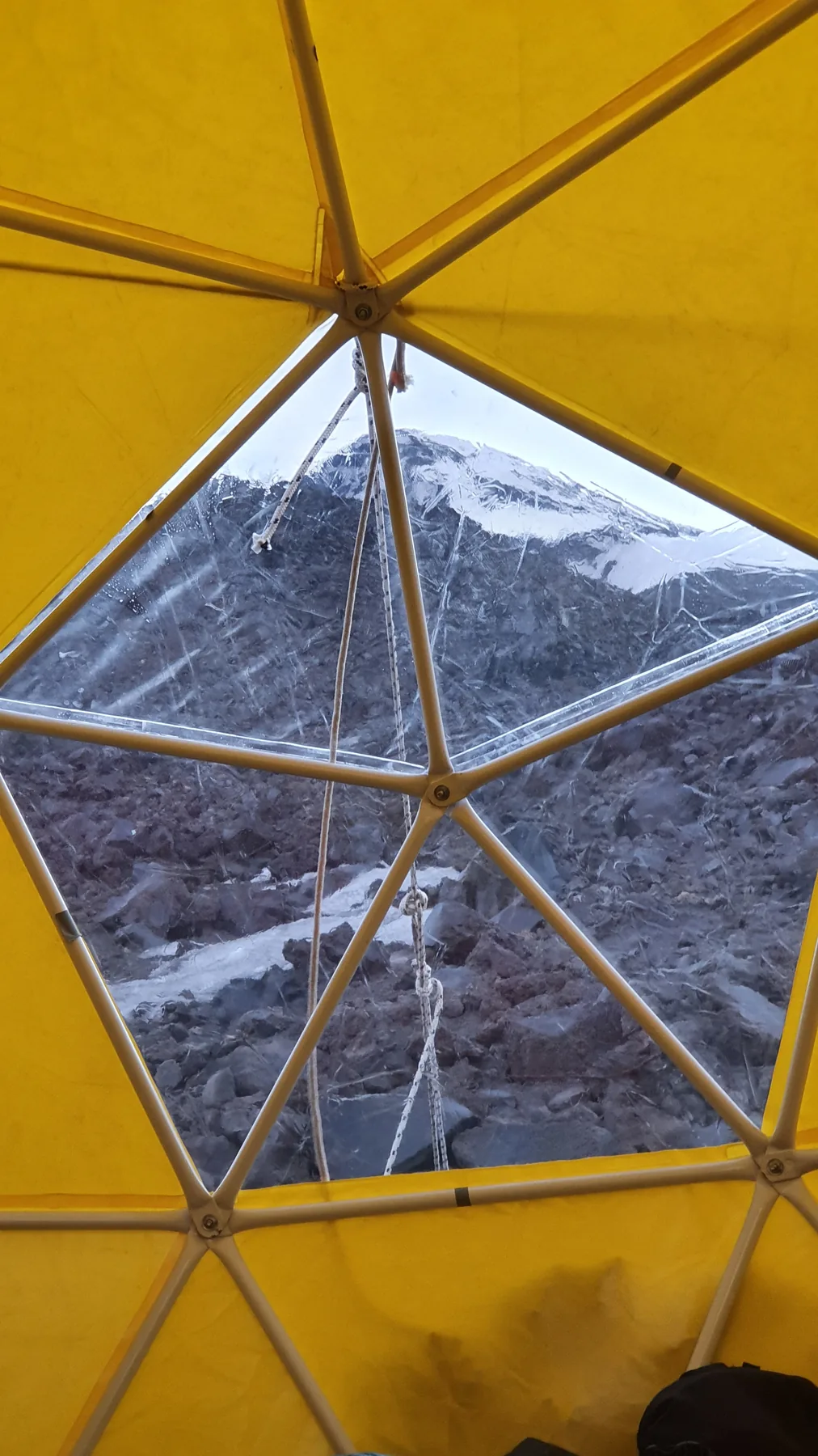 Inside the yellow dome refugio on Lanín at dusk, the framework of the shelter and the mountain visible through the window panel